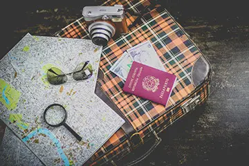 Karierter Reisekoffer mit Pass, Karte, altem Fotoapparat und Flieger-Sonnenbrille darauf
