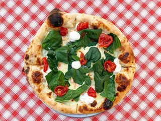 Auf Tisch mit weiß-rot karierter Tischdecke steht Pizza Margherita mit Tomaten, Mozzarella und vielen Basilikumblättern