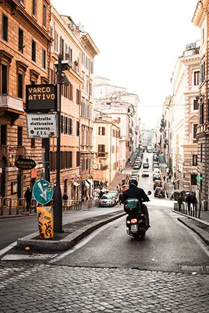 Rollerfahrer fährt Strasse  in italienischer Altstadt runter. Digitales Strassenschild zeigt
